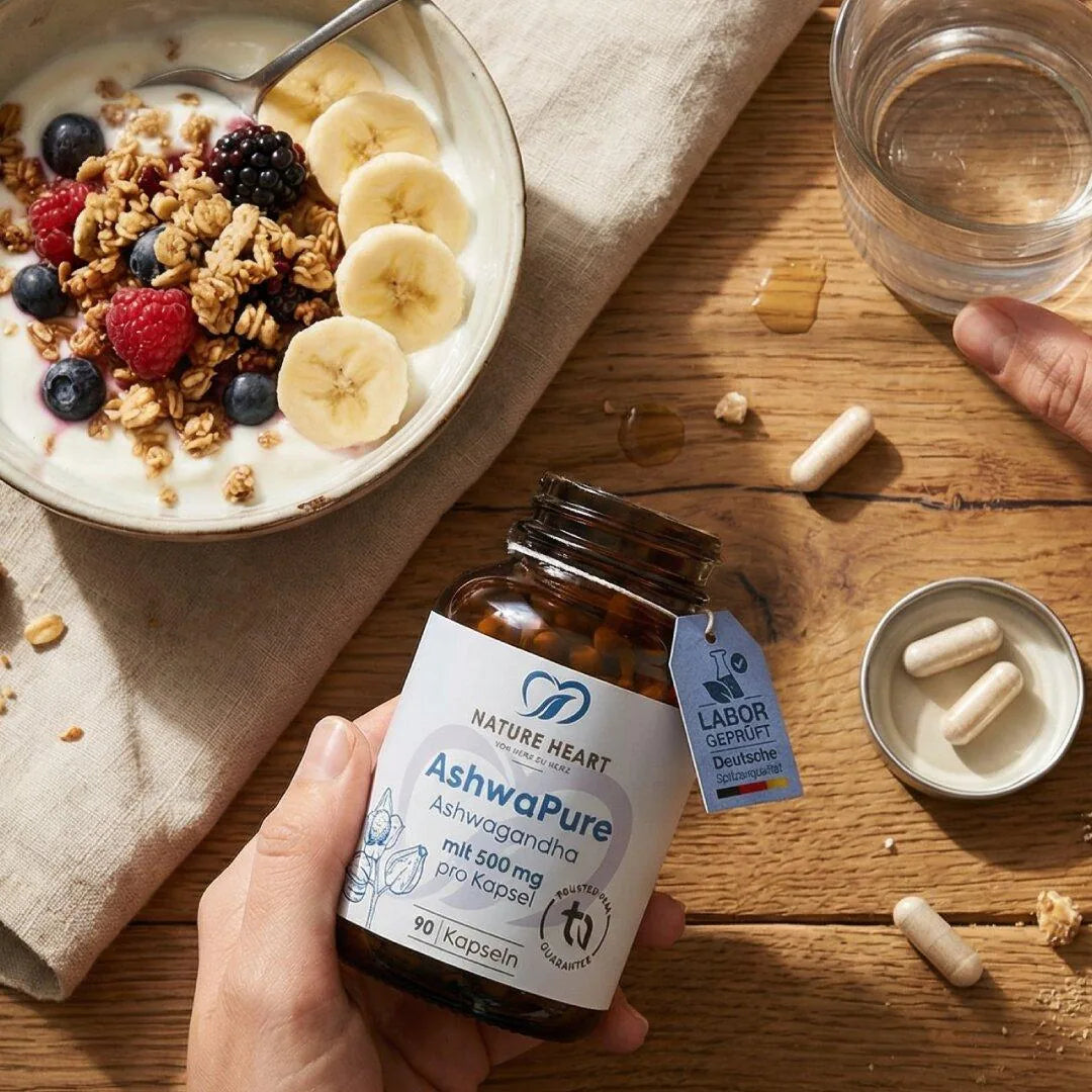 Hand hält eine Flasche AshwaPure Ashwagandha mit 90 Kapseln à 500 mg neben einer Müslischale mit Joghurt, Beeren und Banane