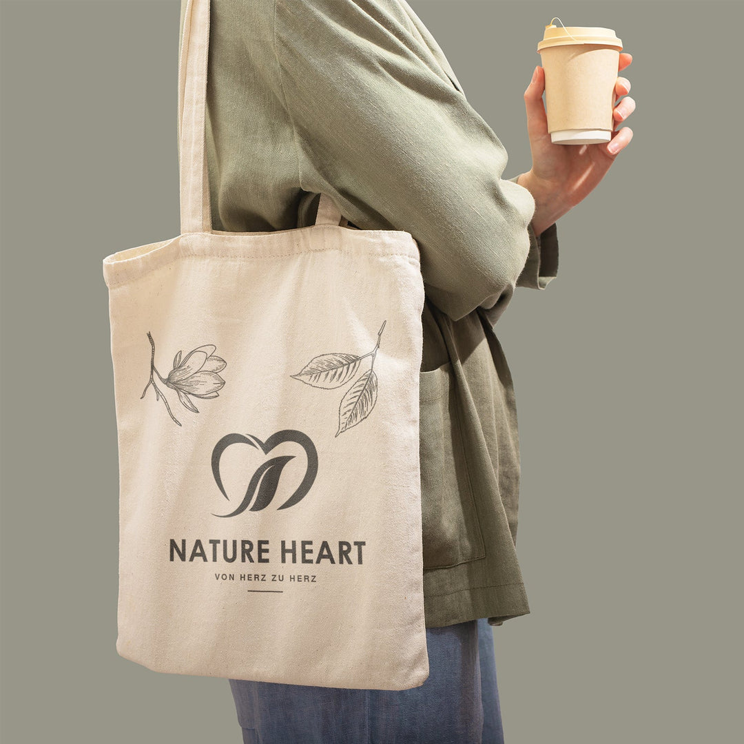 Person trägt die Baumwolltasche Heart über der Schulter und hält einen Kaffeebecher in der Hand