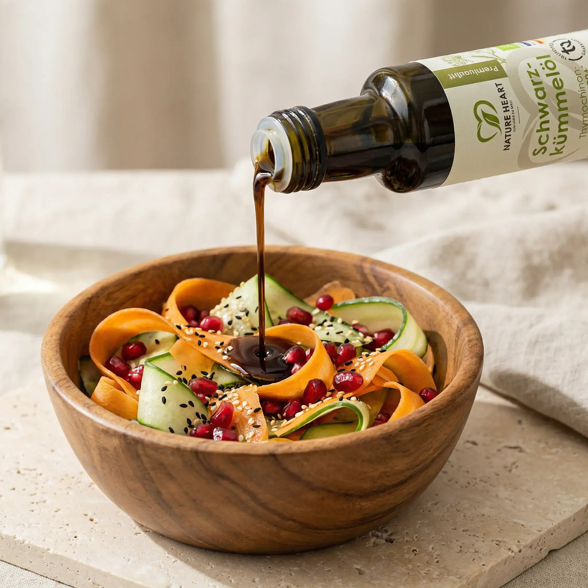 BIO Schwarzkümmelöl 2300+ Thymochinon wird über einen Salat aus Karotten, Gurke und Granatapfelkernen gegossen