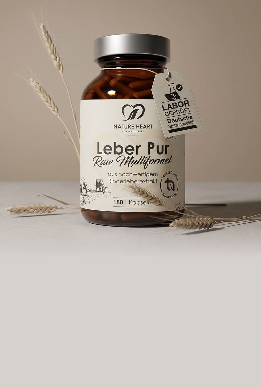 Glasbehälter mit Nature Heart Leber Pur Raw Multiformel aus hochwertigem Rinderleberextrakt, 180 Kapseln, auf neutralem beigem Hintergrund mit Ähren und sichtbarem Labor-geprüft-Tag „Deutsche Spitzenqualität“.