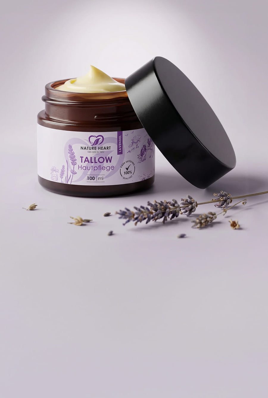 Glasbehälter mit Nature Heart Tallow Hautpflege 100 ml auf hellviolettem Hintergrund, mit sichtbarem Lavendel-Design und geöffnetem schwarzen Deckel neben Lavendelzweigen.