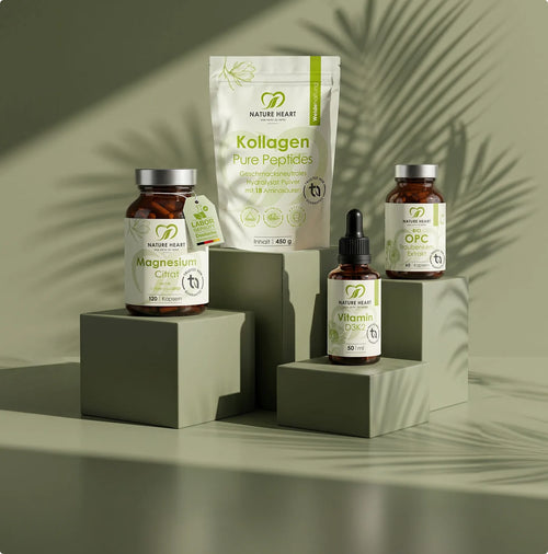 Eine Auswahl an Nature Heart Nahrungsergänzungsmitteln, darunter Magnesium, Kollagen, Vitamin D3K2 und OPC, arrangiert auf olivgrünen Podesten vor einem schattierten Pflanzenhintergrund.