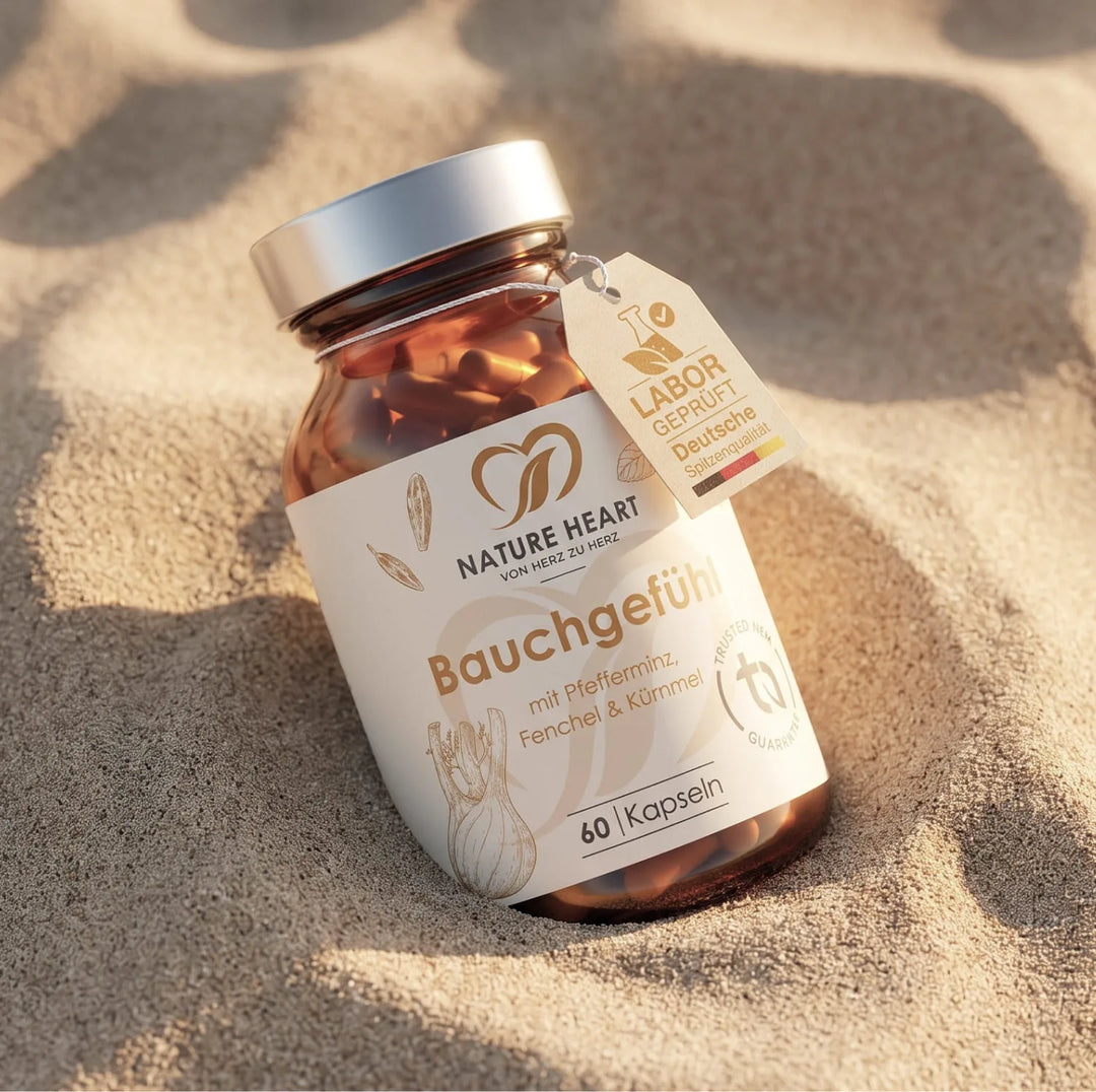 Die Produktflasche Bauchgefühl von Nature Heart mit Pfefferminze, Fenchel und Kümmel ruht im warmen Sand. Ein kleiner, angehängter Papieranhänger trägt die Aufschrift "Labor geprüft - Deutsche Spitzenqualität".
