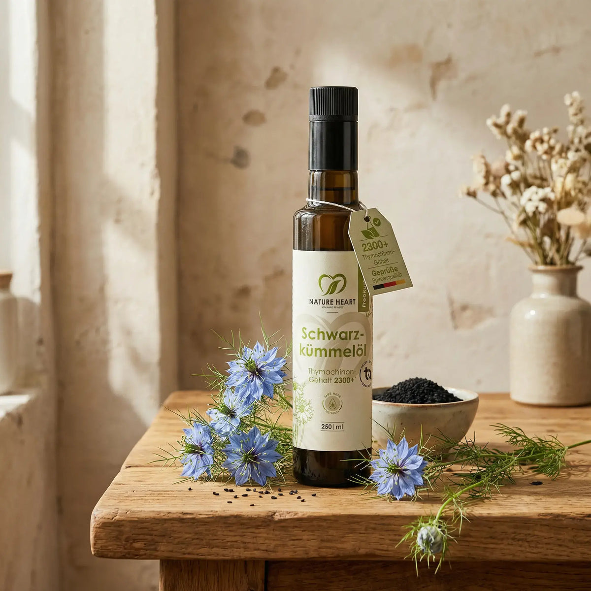 Nature Heart BIO Schwarzkümmelöl 2300+ Thymochinon, 250-ml-Flasche auf Holztisch mit Nigella-Blüten und Samen