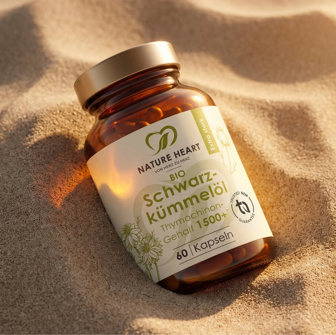Eine Flasche Bio Schwarzkümmelöl Kapseln der Marke Nature Heart ruht in den sanften Wellen einer Sanddüne. Der Aufdruck hebt den extra starken Thymochinon-Gehalt hervor.