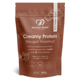 Ein brauner Standbodenbeutel mit Nature Heart Creamy Protein Pulver, Geschmacksrichtung Nougat Hazelnut, 450g Inhalt. Die freigestellte Verpackung zeigt Illustrationen von Haselnüssen und Schokoladenstücken.