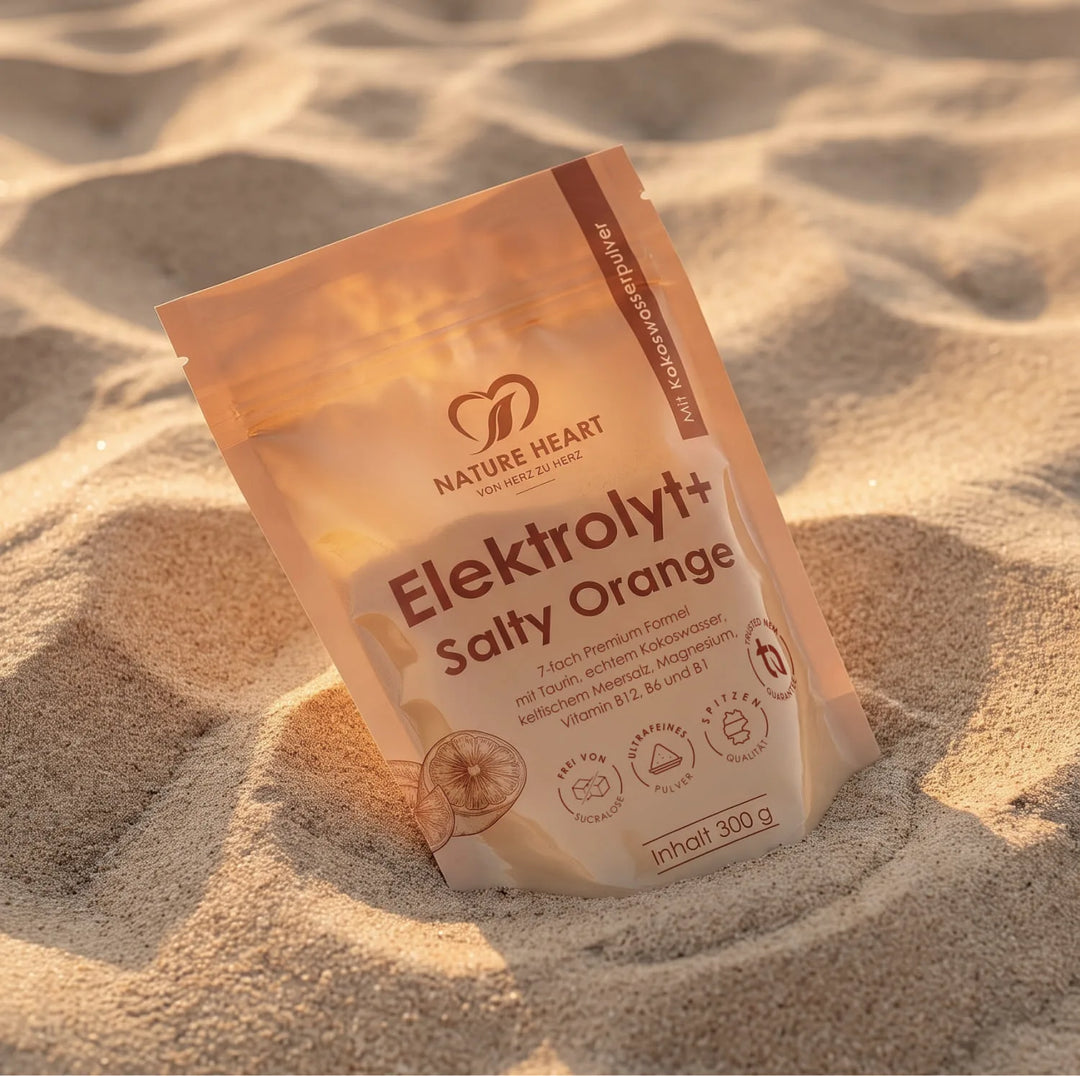 Ein stehender Standbodenbeutel mit Elektrolyt+ Salty Orange Pulver von Nature Heart, platziert inmitten einer sonnenbeschienenen Sandlandschaft. Die Verpackung zeigt dezente Orangen-Illustrationen.