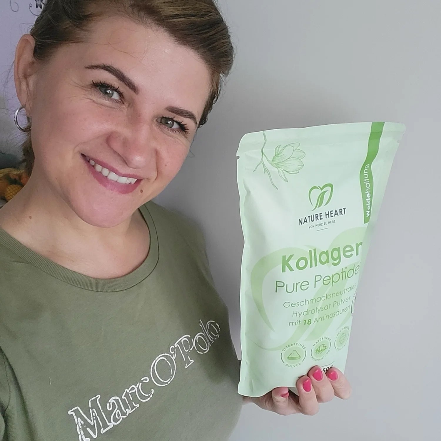 Eine lächelnde Frau im grünen T-Shirt hält eine Packung Nature Heart Kollagen Pure Peptides in der Hand.