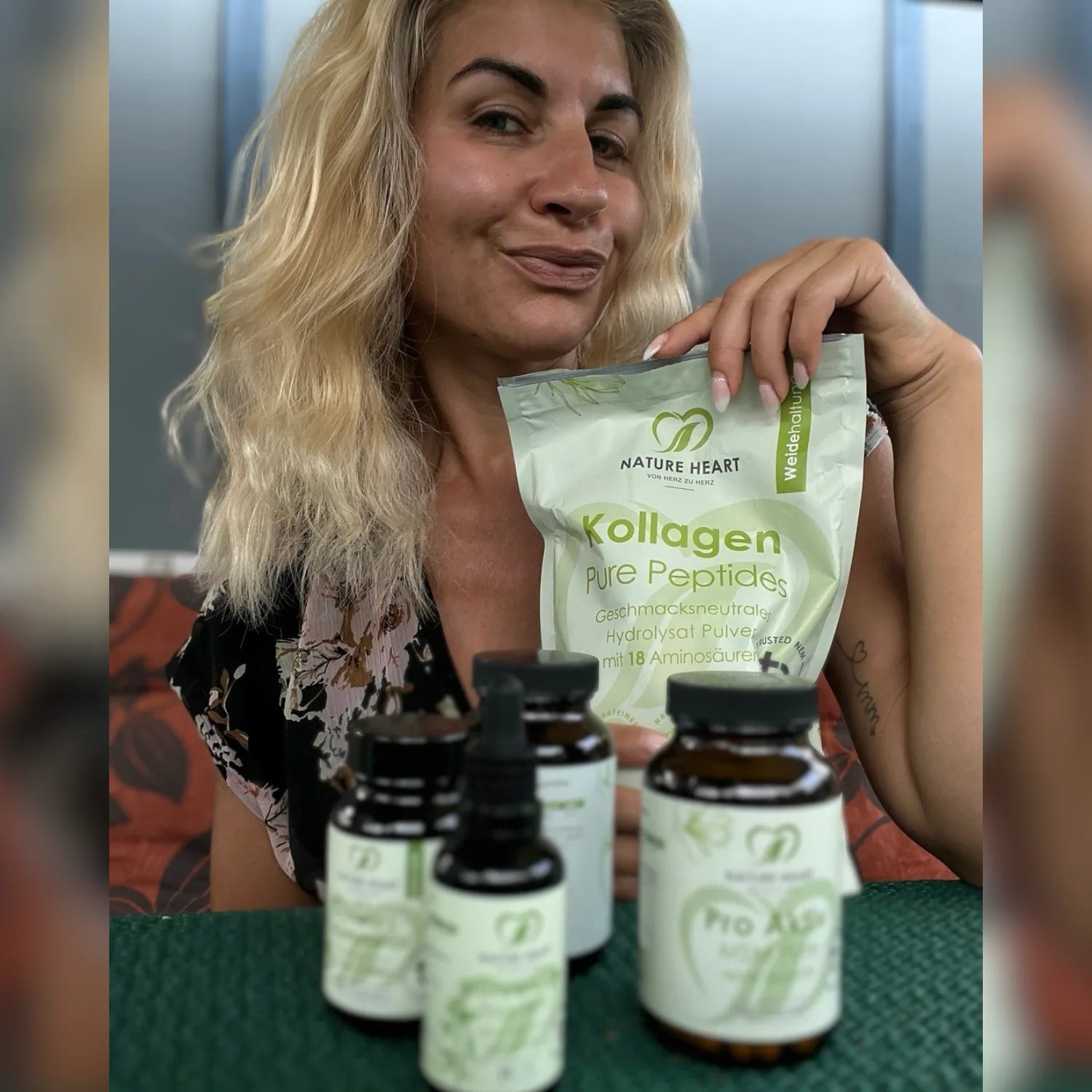 Eine lächelnde blonde Frau hält eine Packung Nature Heart Kollagen Pure Peptides, während im Vordergrund verschiedene Produktflaschen auf dem Tisch stehen.