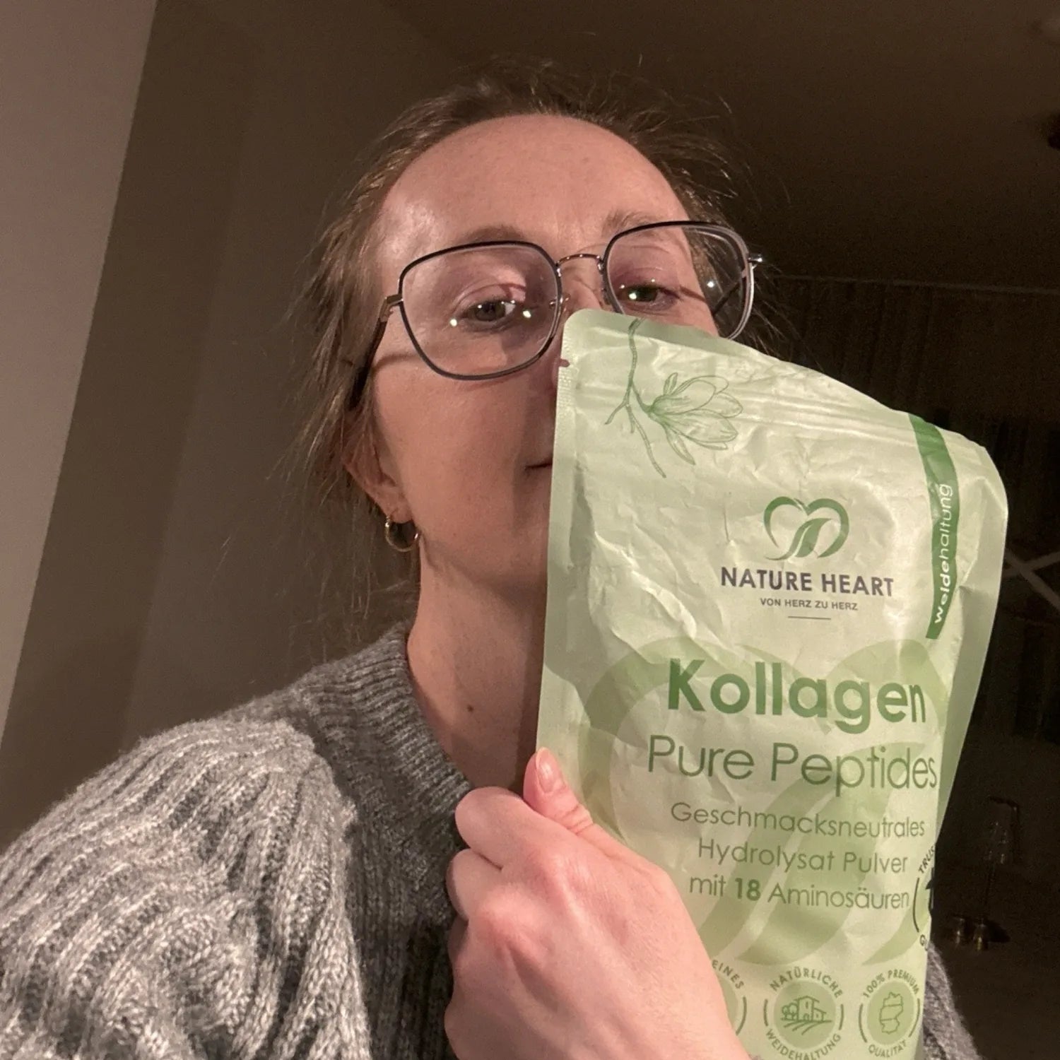 Eine Frau hält einen Beutel Nature Heart Kollagen Pure Peptides Pulver vor ihr Gesicht.