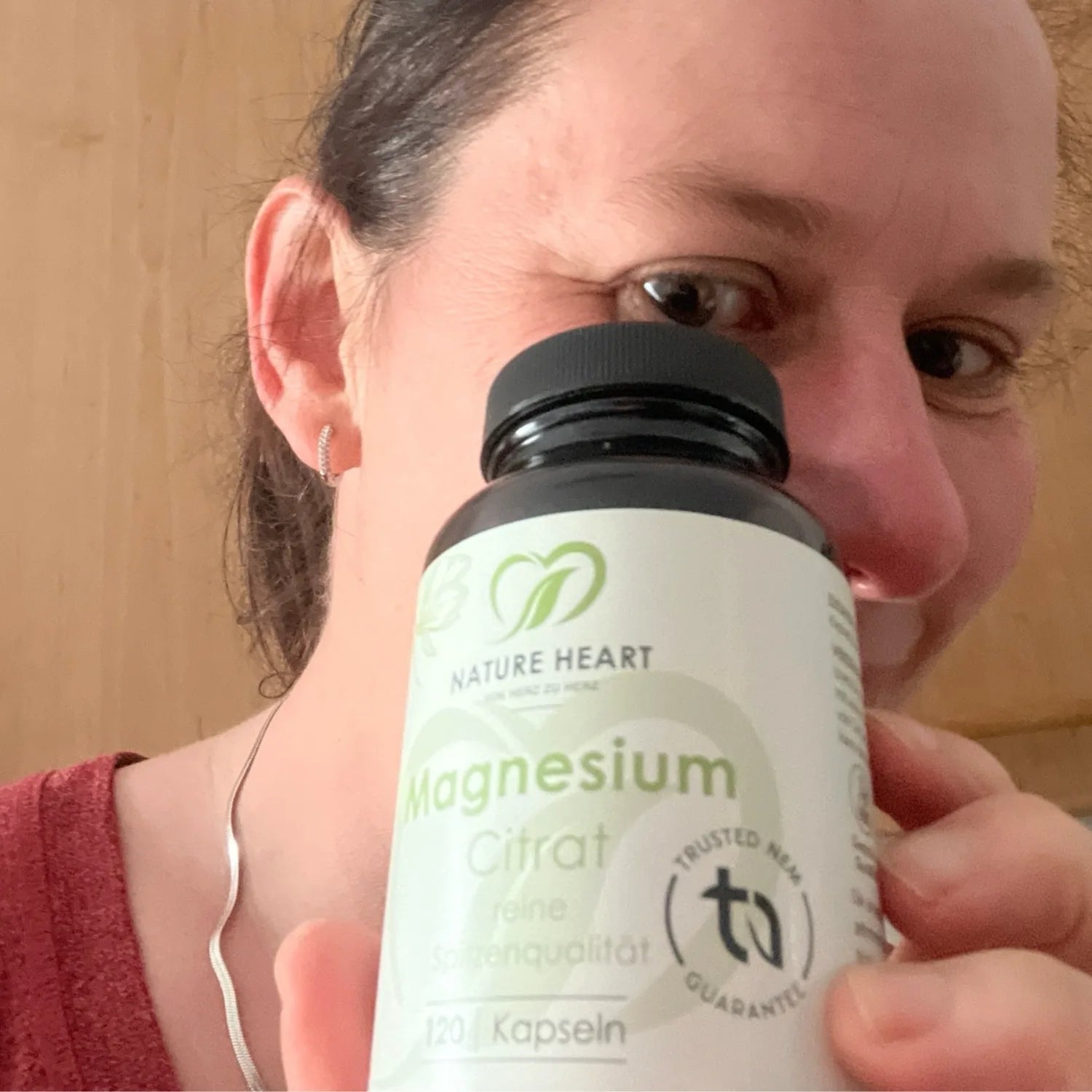 Eine Frau hält ein Glas Nature Heart Magnesium Citrat Kapseln dicht vor ihr Gesicht, sodass ein Auge knapp verdeckt wird.