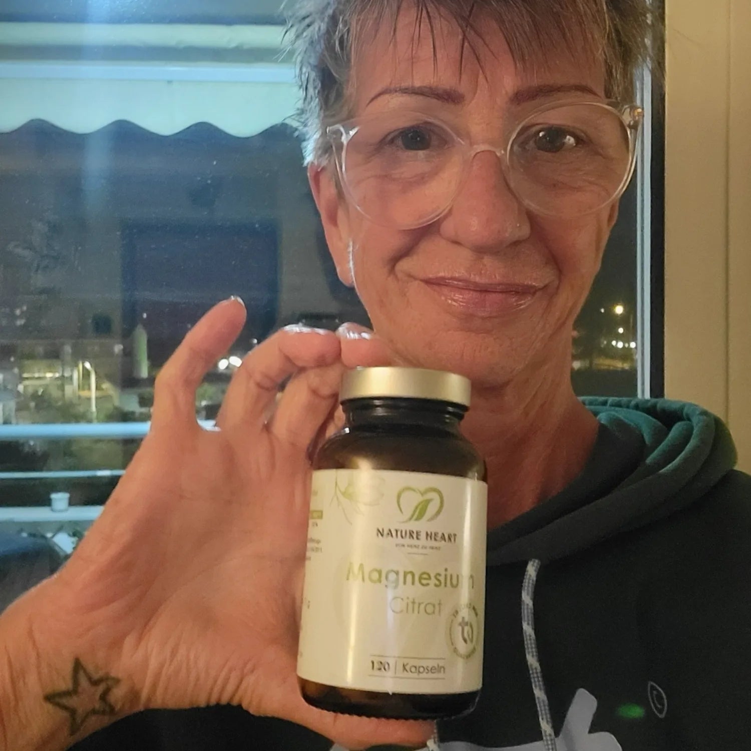 Eine Frau mit Brille präsentiert ein Glas Nature Heart Magnesium Citrat Kapseln.
