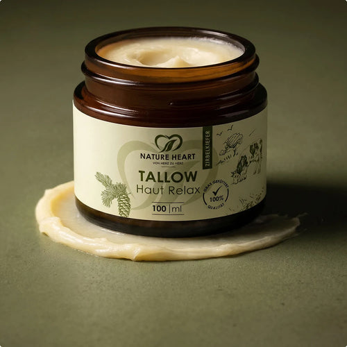 Ein geöffneter Tiegel der Nature Heart Tallow Haut-Relax Creme steht auf einer kleinen Menge der cremig-weißen Textur vor einem olivgrünen Hintergrund.