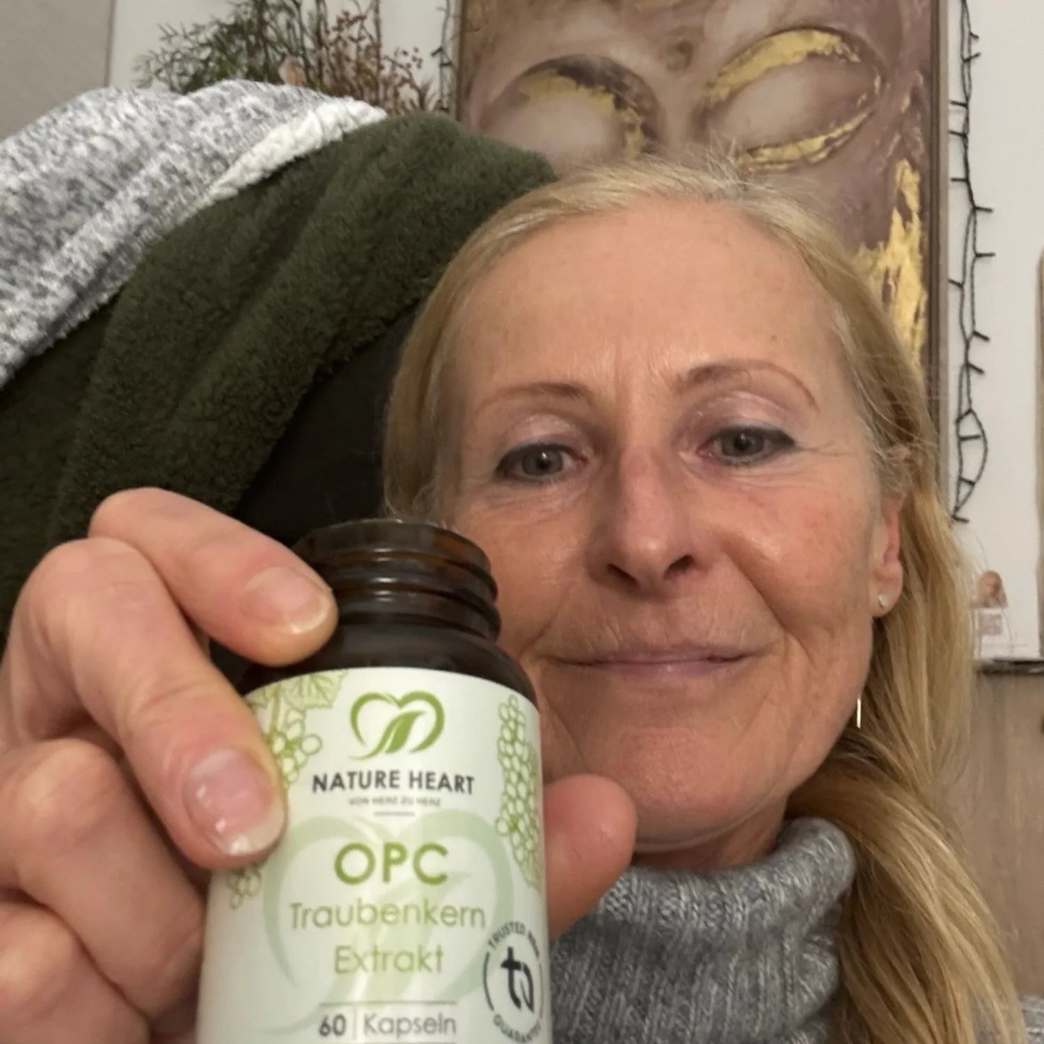 Eine blonde Frau zeigt ein geöffnetes Glas Nature Heart OPC Traubenkern Extrakt Kapseln.