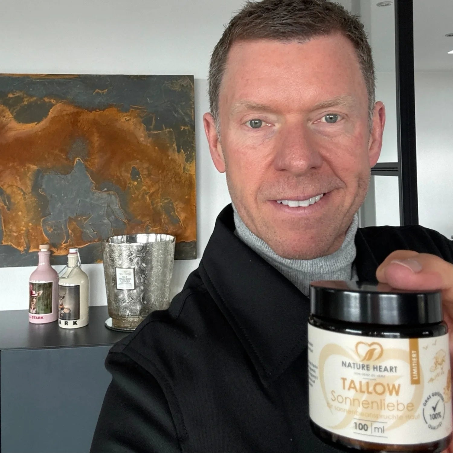 Ein lächelnder Mann hält einen Tiegel Nature Heart Tallow Sonnenliebe für sonnenbeanspruchte Haut in die Kamera.