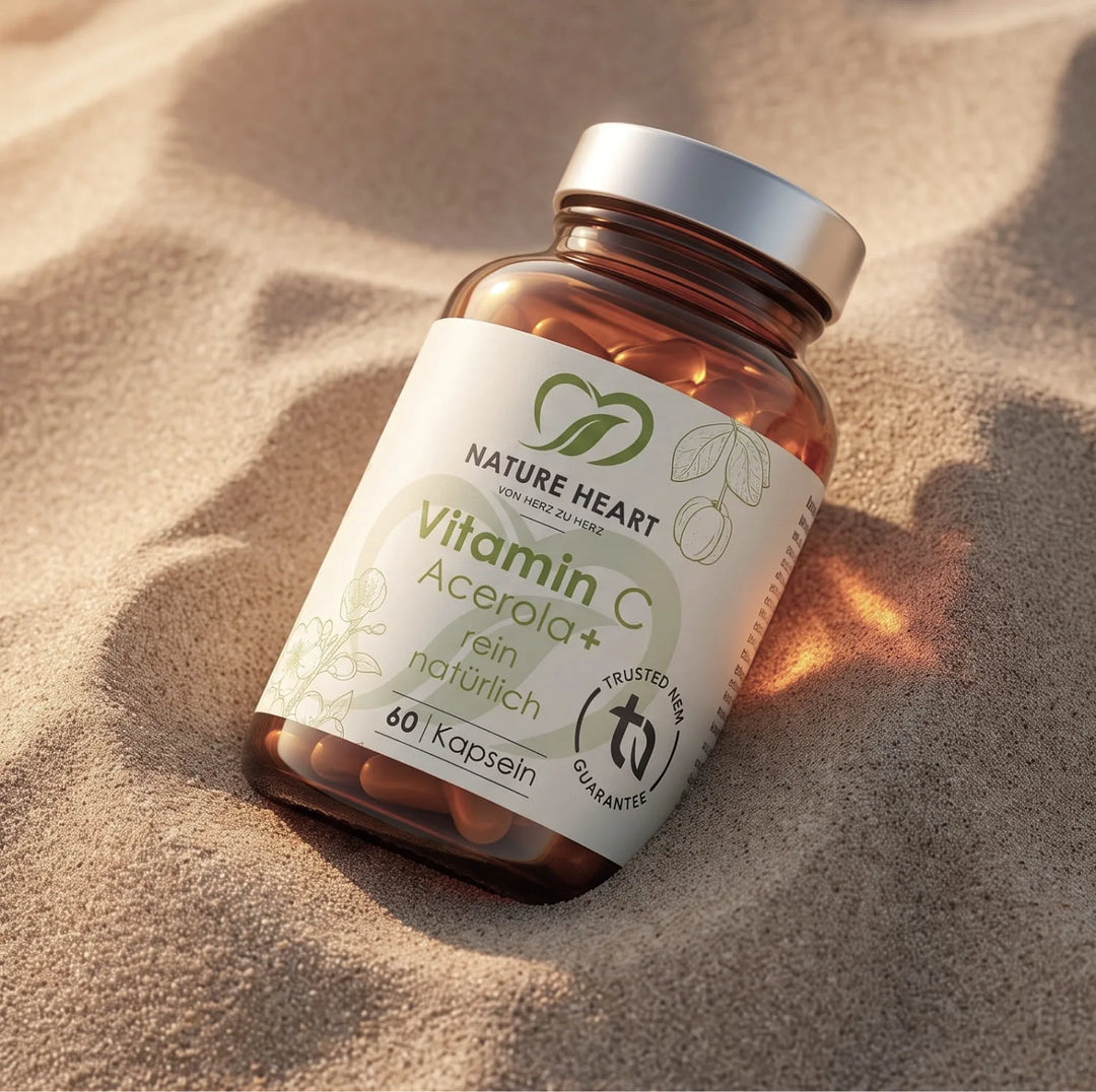 Eine Braunglasflasche Vitamin C Acerola+ von Nature Heart liegt im hellen Sand. Das Etikett betont die rein natürliche Zusammensetzung des Nahrungsergänzungsmittels.