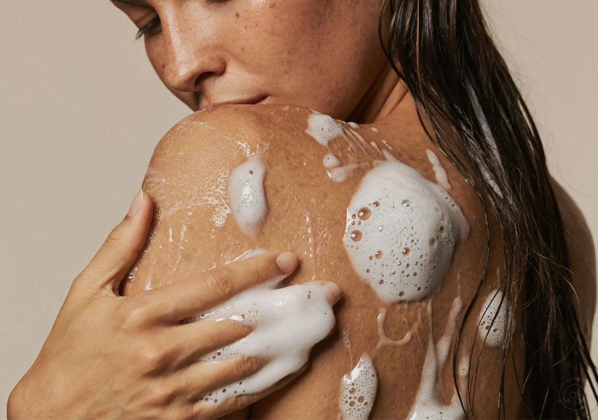 Frau mit nassem Haar verteilt cremigen Schaum auf ihrer Schulter, Symbolbild für die Kategorie Naturkosmetik