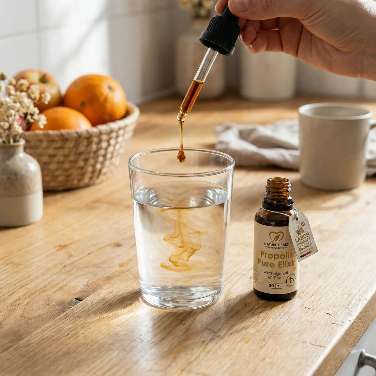 Propolis Pure Elixir wird mit der Pipette in ein Glas Wasser getropft, daneben die 20-ml-Flasche mit 80 % vol. Alkoholgehalt