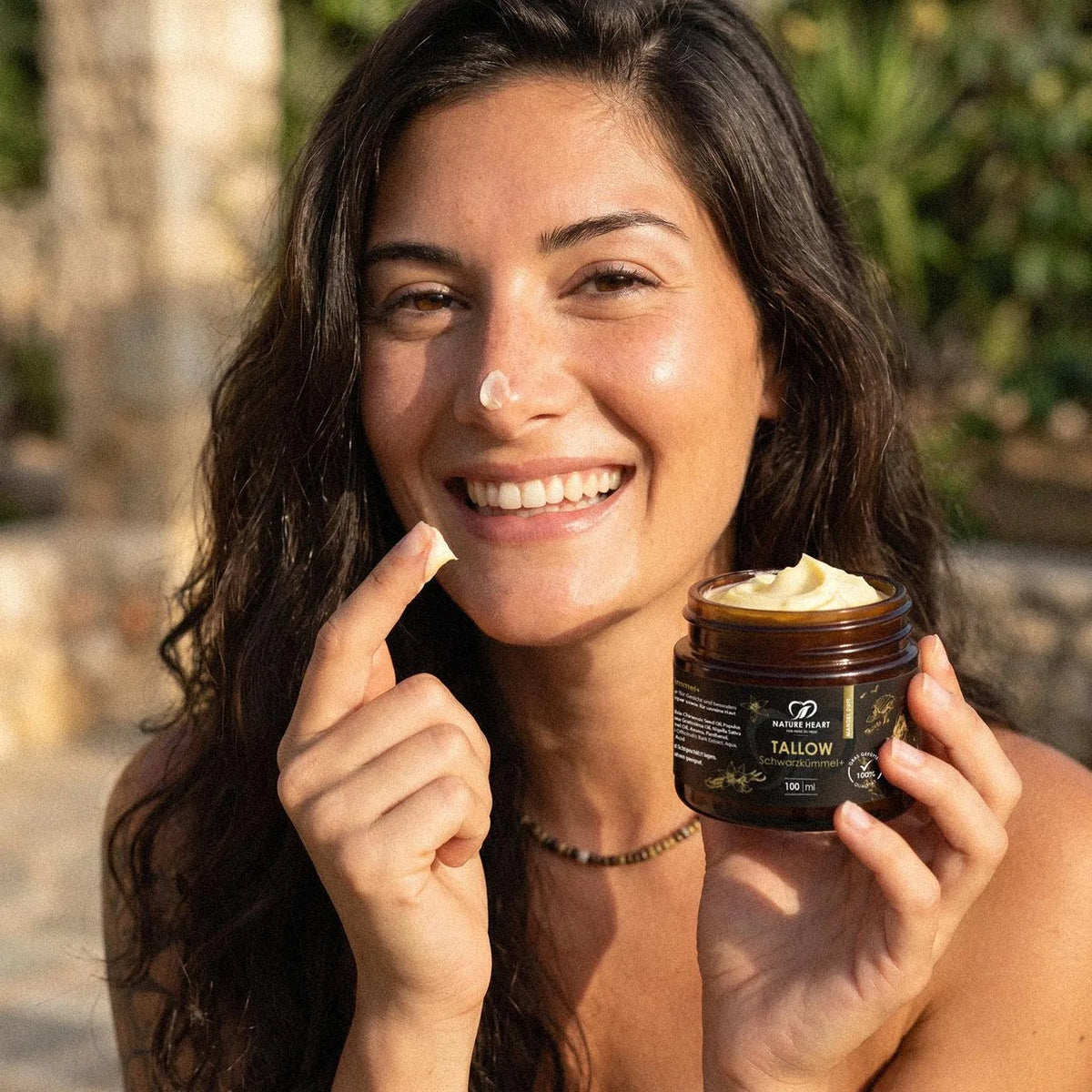 Lachende Frau mit einem Klecks Creme auf der Nase hält den geöffneten Tiegel Tallow Schwarzkümmel+ 100 ml in die Kamera
