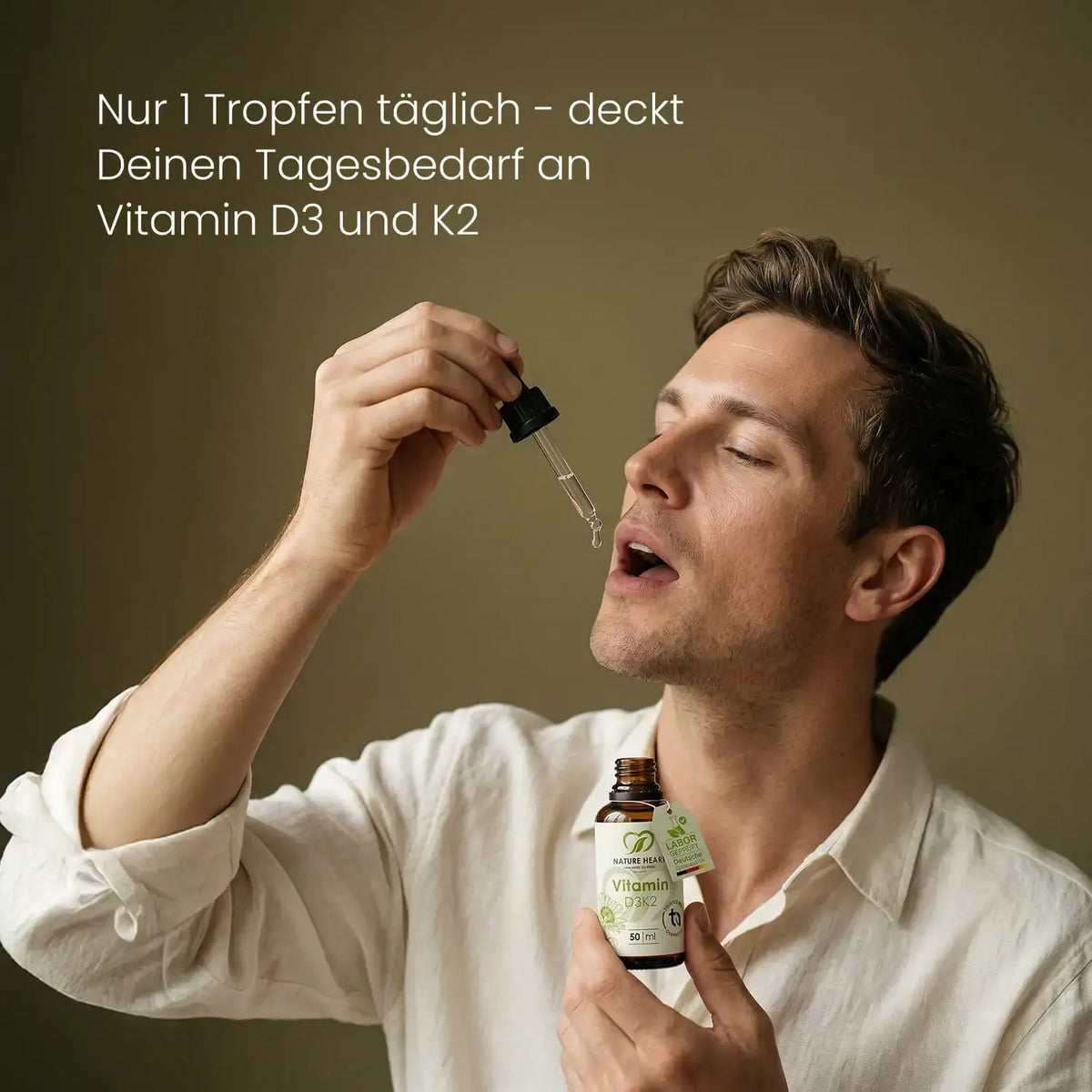 Mann tropft sich Vitamin D3K2 Tropfen mit der Pipette in den Mund und hält die 50-ml-Flasche, Hinweis: 1 Tropfen täglich